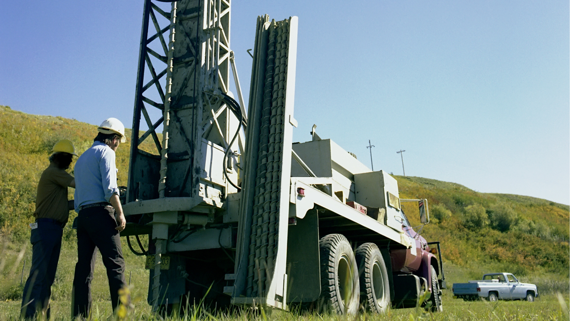 Drill rig on a geotechnical investigation site with a technician logging borehole data on a tablet
